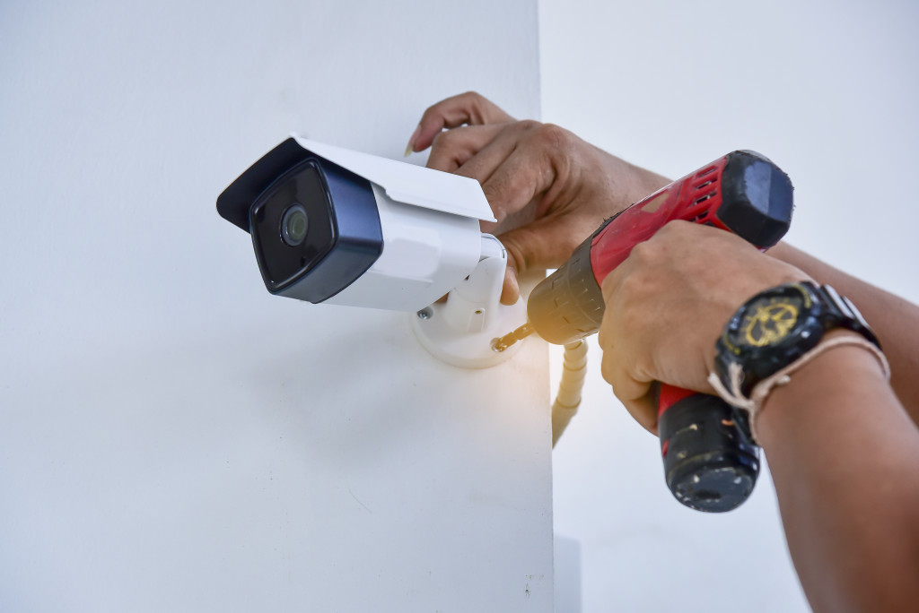 person installing a CCTV camera in a white wall corner